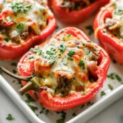 Philly steak and cheese stuffed peppers in a white baking dish, topped with melted mozzarella and fresh parsley.