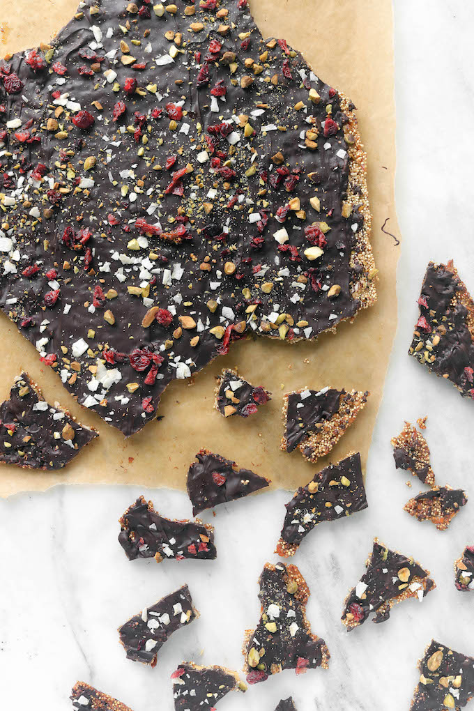 Superfood Dark Chocolate Quinoa Bark on brown parchment paper. Scattered pieces of quinoa bark are arranged on a marble countertop.