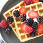 Two Belgian Spelt Waffles on a gray plate. Waffles topped with berries and vanilla yogurt.