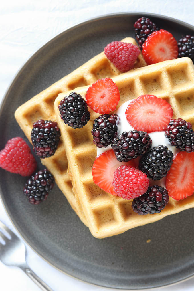 Two Belgian Spelt Waffles on a gray plate. Waffles topped with berries and vanilla yogurt.