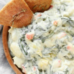 Slow Cooker Spinach Artichoke Dip in a wooden bowl sitting on a white marble counter.