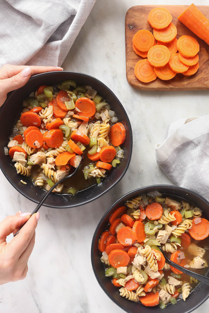 Whole Grain Chicken Noodle Soup in 2 black bowls on a white marble countertop.