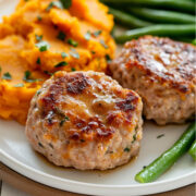 Close-up of two browned mini turkey meatloaves served with mashed sweet potatoes and crisp green beans on a white plate.