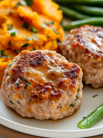 Close-up of two browned mini turkey meatloaves served with mashed sweet potatoes and crisp green beans on a white plate.