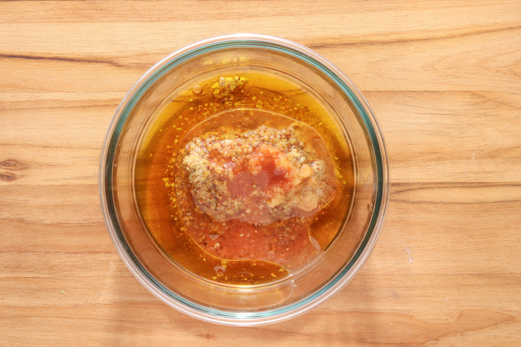 Clear glass bowl filled with honey, whole grain mustard, olive oil, garlic, vinegar, and hot sauce before being whisked into a marinade.