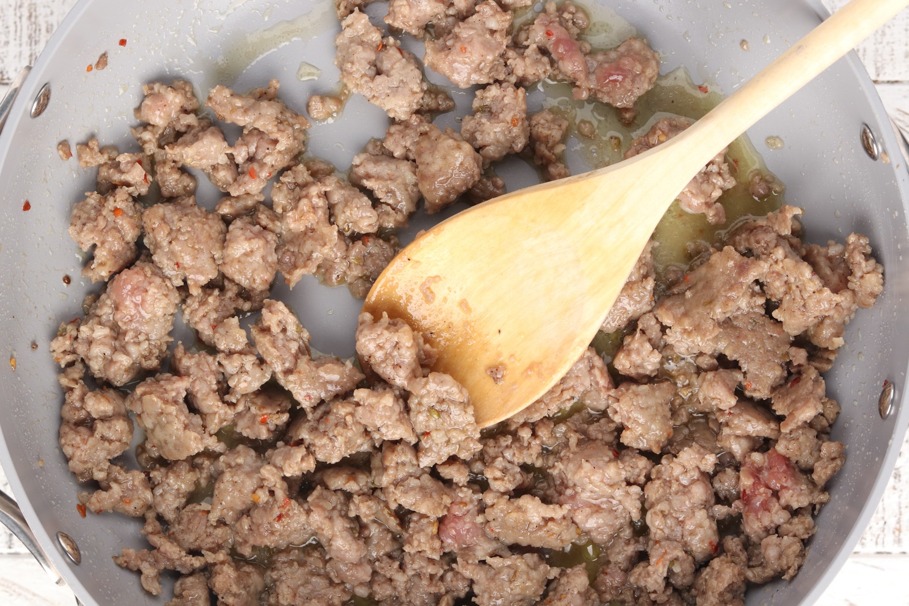 Ground breakfast sausage cooking in a skillet with a wooden spoon, being browned and crumbled for making freezer breakfast sandwiches.
