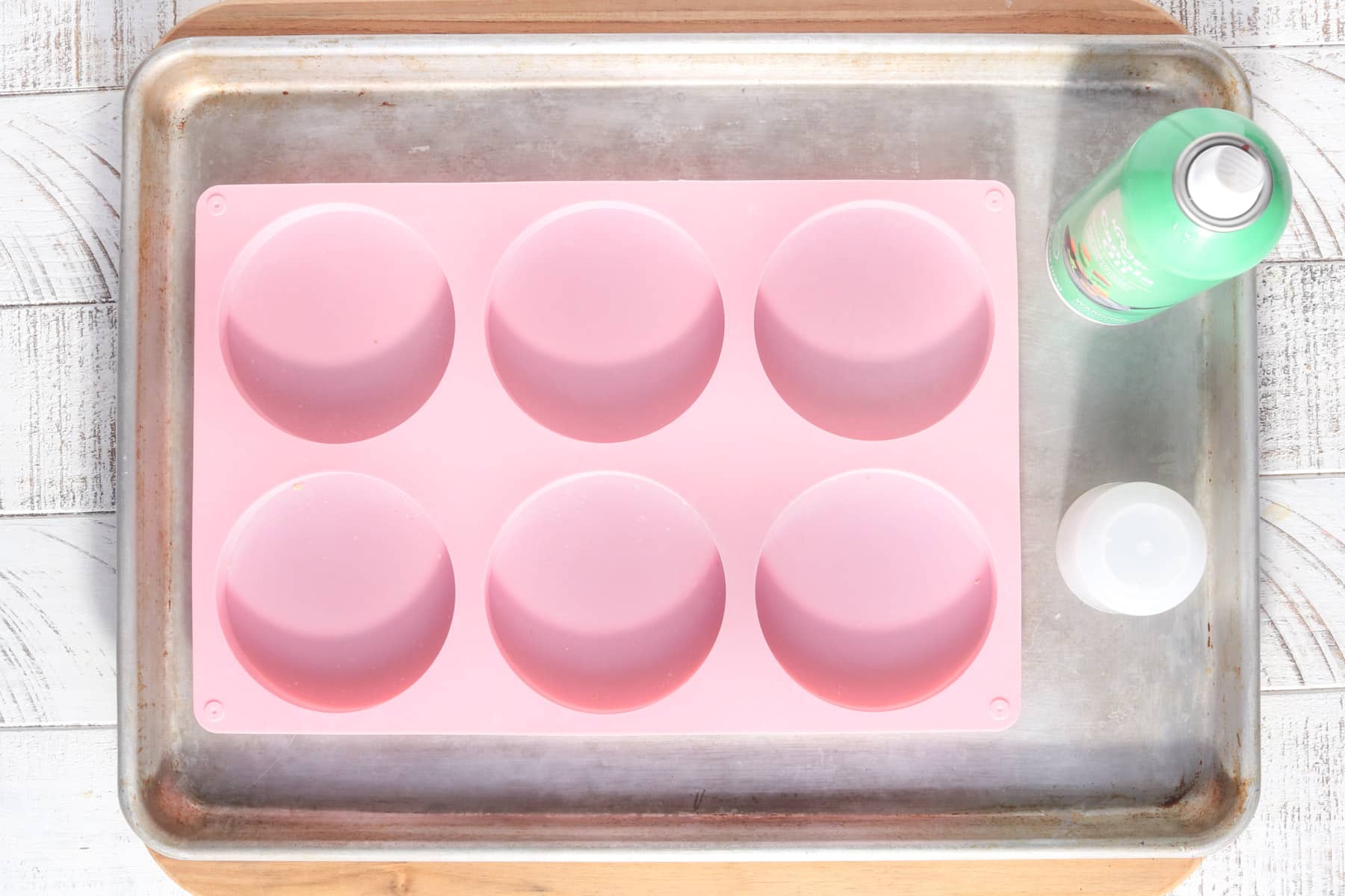 Overhead view of an empty pink silicone mold on a sheet pan with cooking spray nearby, showing the first step in preparing egg rounds for freezer breakfast sandwiches.