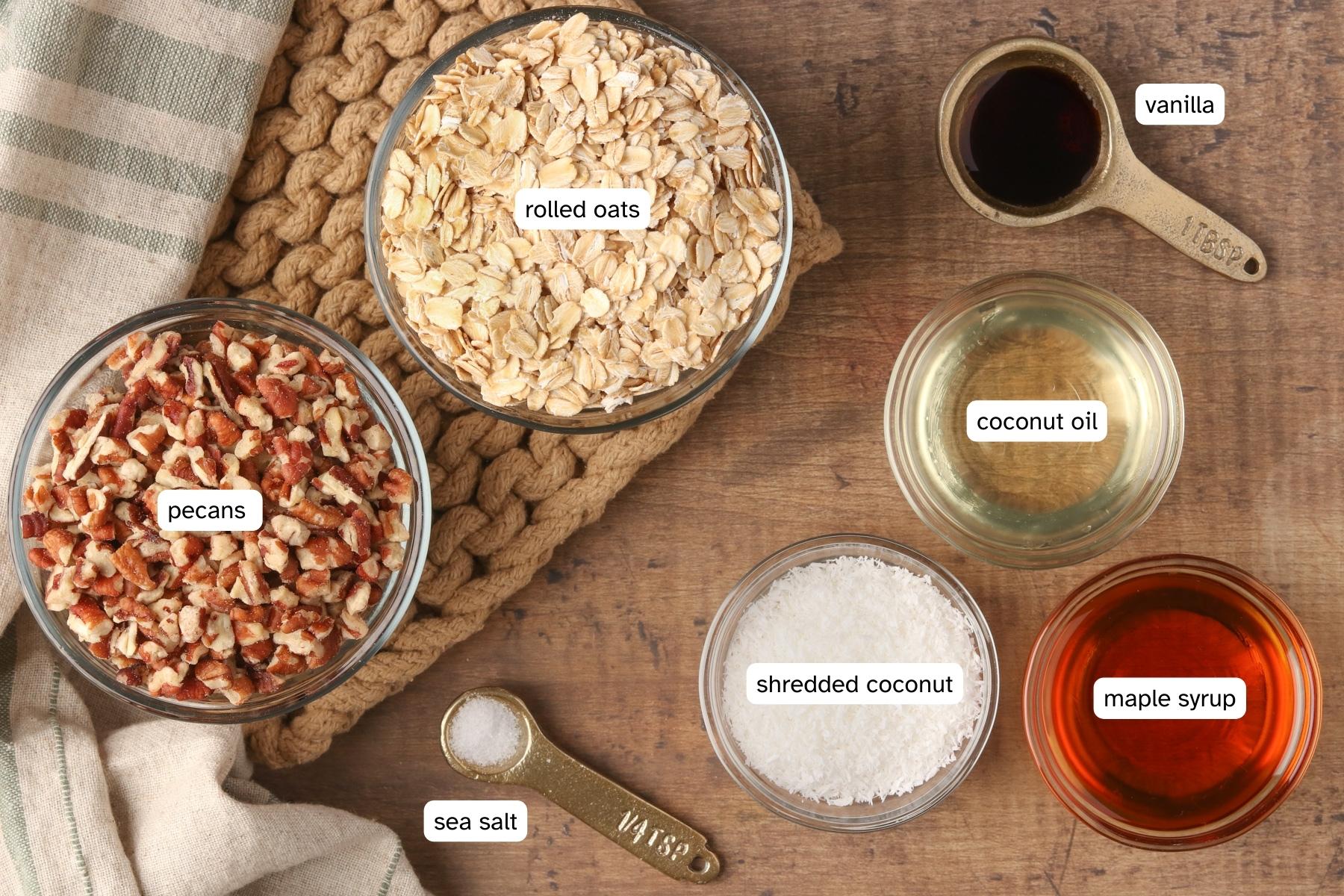 Ingredients to make crunchy chunky granola - rolled oats, pecans, salt, coconut, maple syrup, coconut oil and vanilla.
