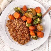 Pecan crusted pork chops with balsamic roasted veggies on a white plate.