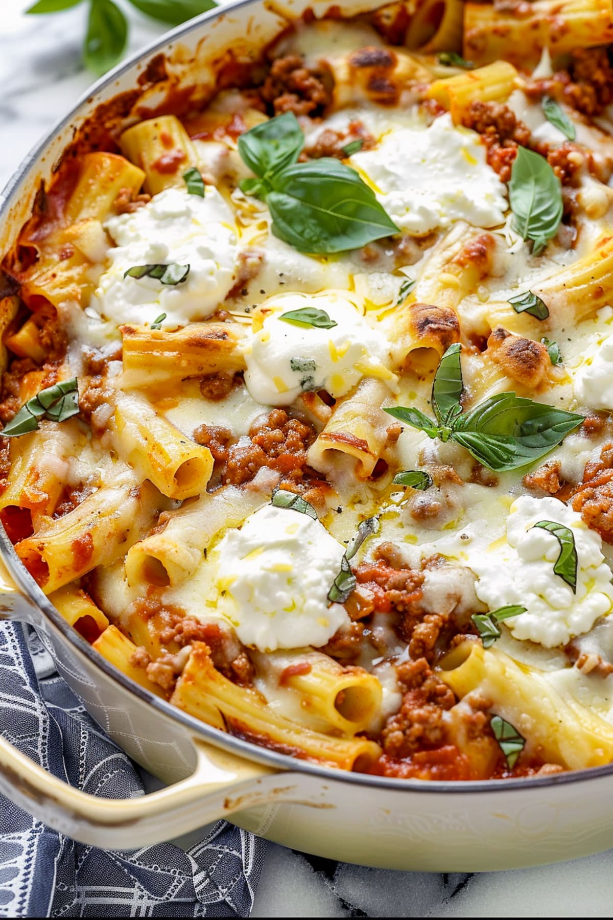 Creamy ricotta and sausage pasta with rigatoni, marinara sauce, melted mozzarella, and fresh basil in a white skillet.