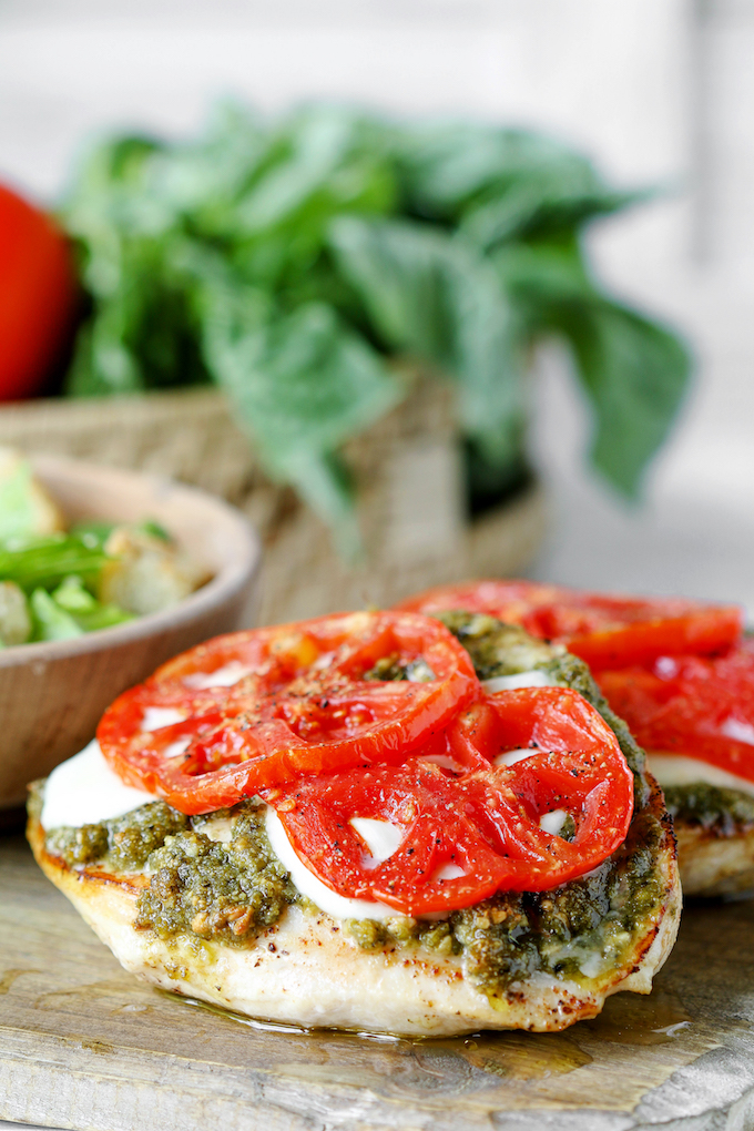 4 Ingredient Pesto Chicken Bake paired with a garden salad. A basket of basil and fresh tomatoes is in the background.