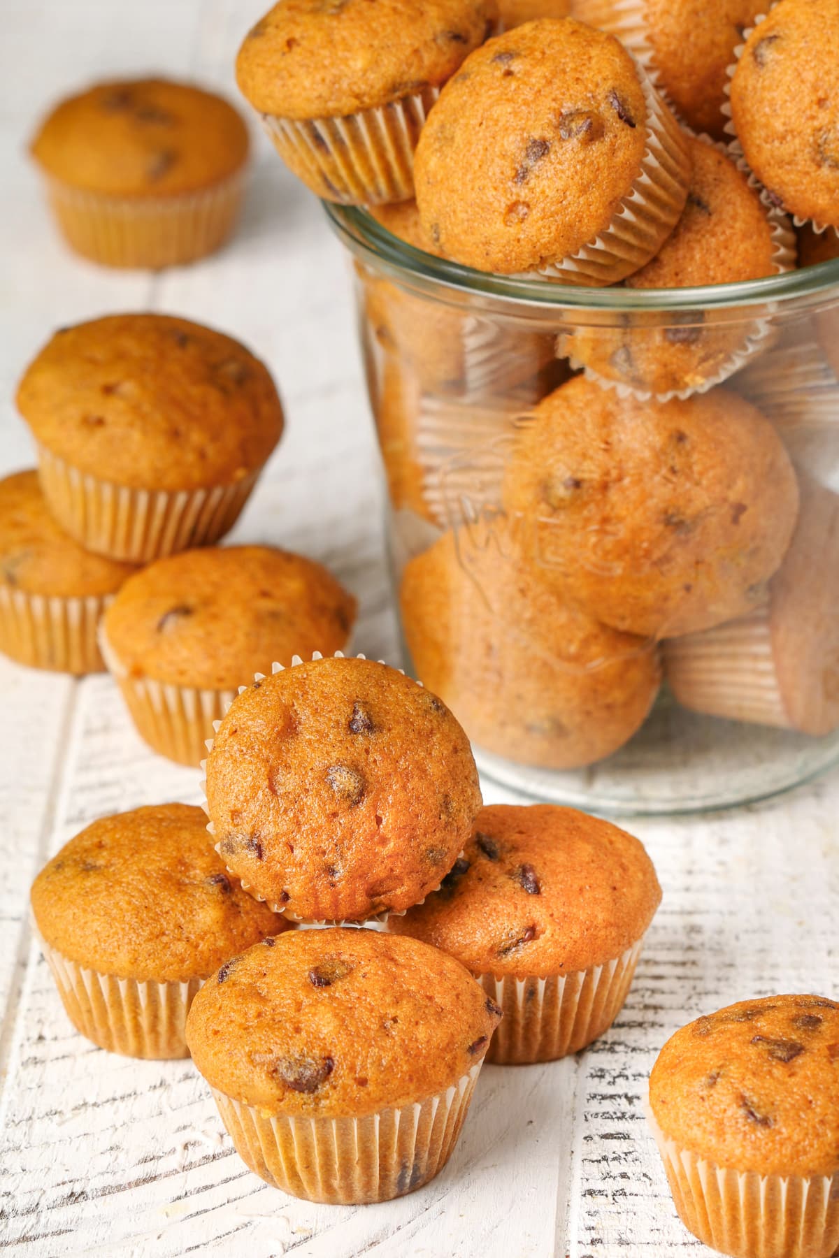 Mini Chocolate Chip Pumpkin Muffins spilling out of a glass jar onto a white countertop.