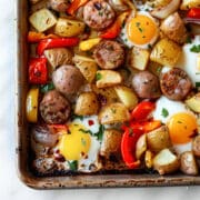 Sheet pan breakfast with roasted potatoes, sliced sausage, bell peppers, and onions baked with eggs, finished with fresh herbs and crispy edges.