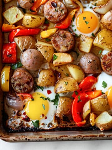 Sheet pan breakfast with roasted potatoes, sliced sausage, bell peppers, and onions baked with eggs, finished with fresh herbs and crispy edges.