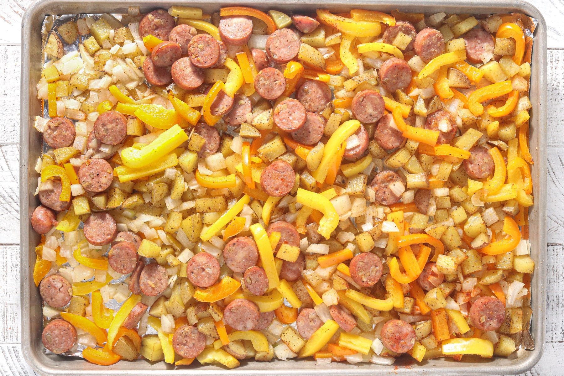 Roasted sheet pan potatoes with chicken sausage, bell peppers, and onions before eggs are added.