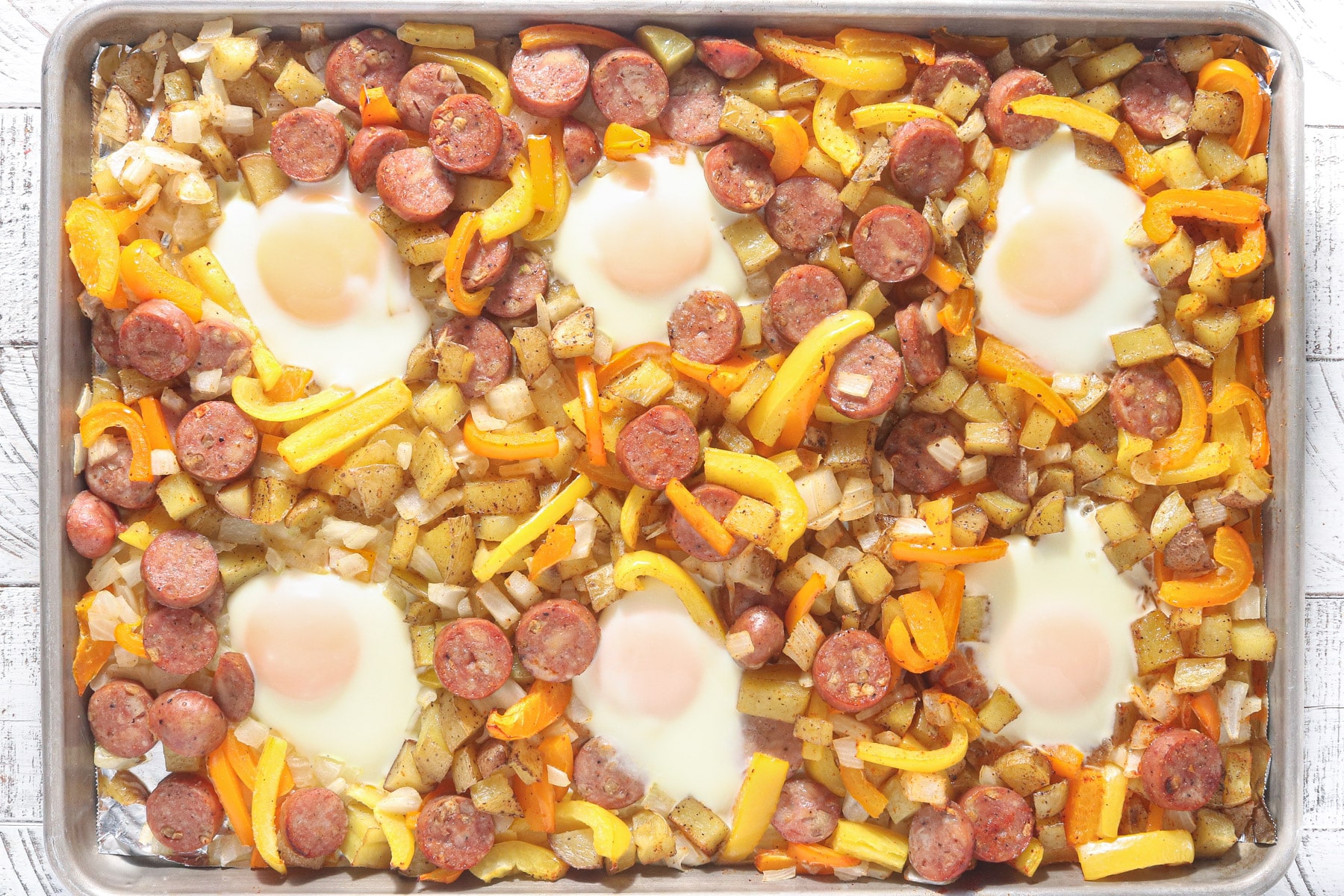 Eggs baked on a sheet pan with roasted potatoes, chicken sausage, bell peppers, and onions.