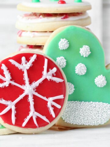 2 cookies decorated with royal icing made without meringue powder. One red circle with a snowflake and one green mitten with white dots made out of sprinkles.