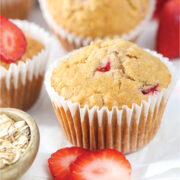 Homemade strawberry oatmeal muffins with fresh strawberries and rolled oats on a white parchment surface.