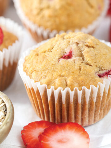 Homemade strawberry oatmeal muffins with fresh strawberries and rolled oats on a white parchment surface.