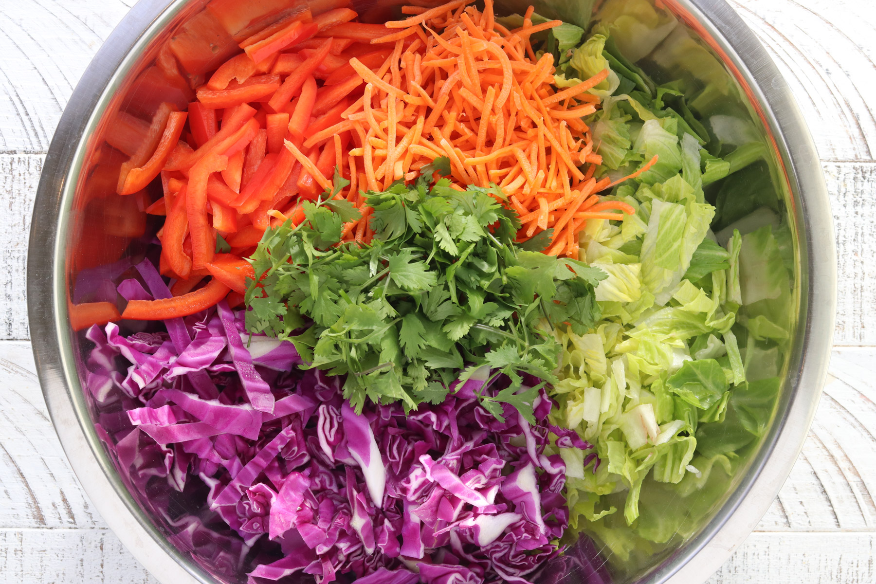 Ingredients for Thai chicken salad including romaine, red cabbage, carrots, bell pepper, and cilantro in a mixing bowl.