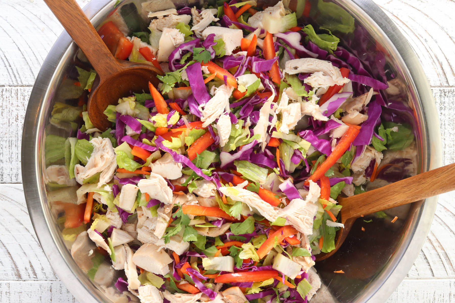 Thai chicken salad with shredded chicken, cabbage, carrots, bell pepper, and romaine tossed together in a bowl.