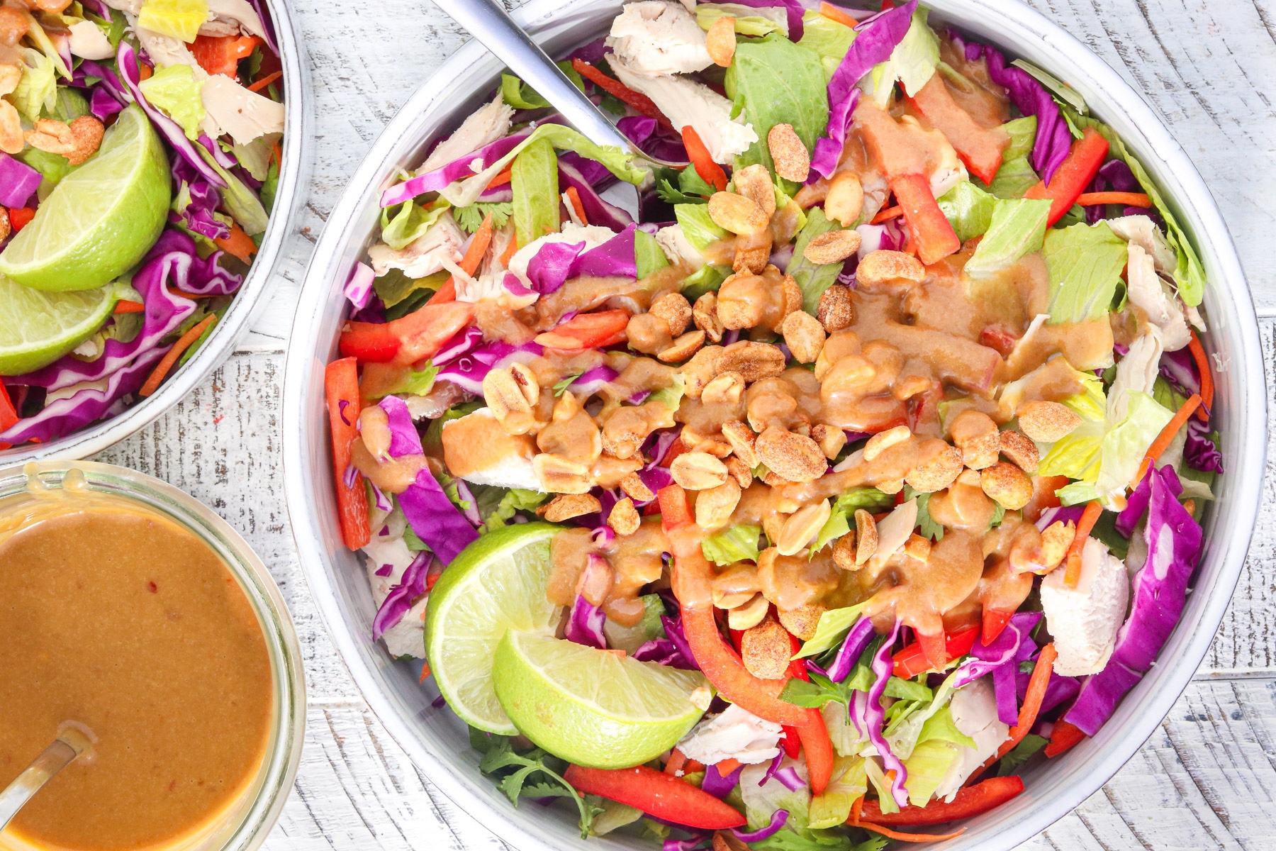 Crunchy Thai chicken salad topped with peanut dressing, chopped peanuts, and fresh lime wedges.
