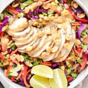 Thai chicken crunch salad with sliced grilled chicken, cabbage, carrots, red pepper, cilantro, peanuts, and creamy peanut dressing with lime wedges.