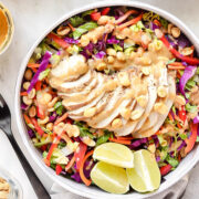 Thai chicken crunch salad with sliced grilled chicken, cabbage, carrots, red pepper, cilantro, peanuts, and creamy peanut dressing with lime wedges.