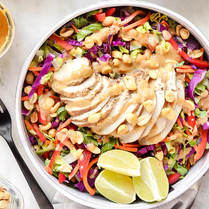 Thai chicken crunch salad with sliced grilled chicken, cabbage, carrots, red pepper, cilantro, peanuts, and creamy peanut dressing with lime wedges.