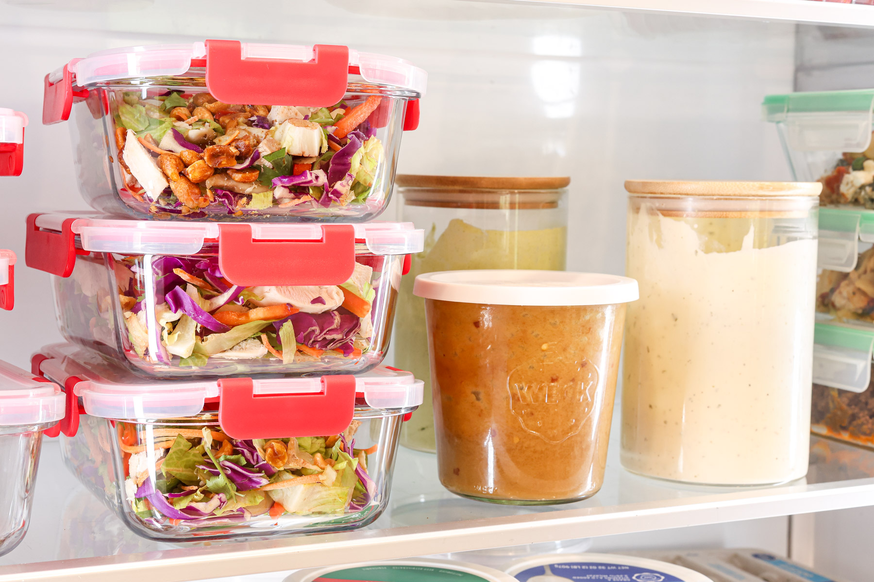 Meal prep containers of crunchy Thai chicken salad with cabbage, carrots, shredded chicken, and peanut dressing stored in the refrigerator.