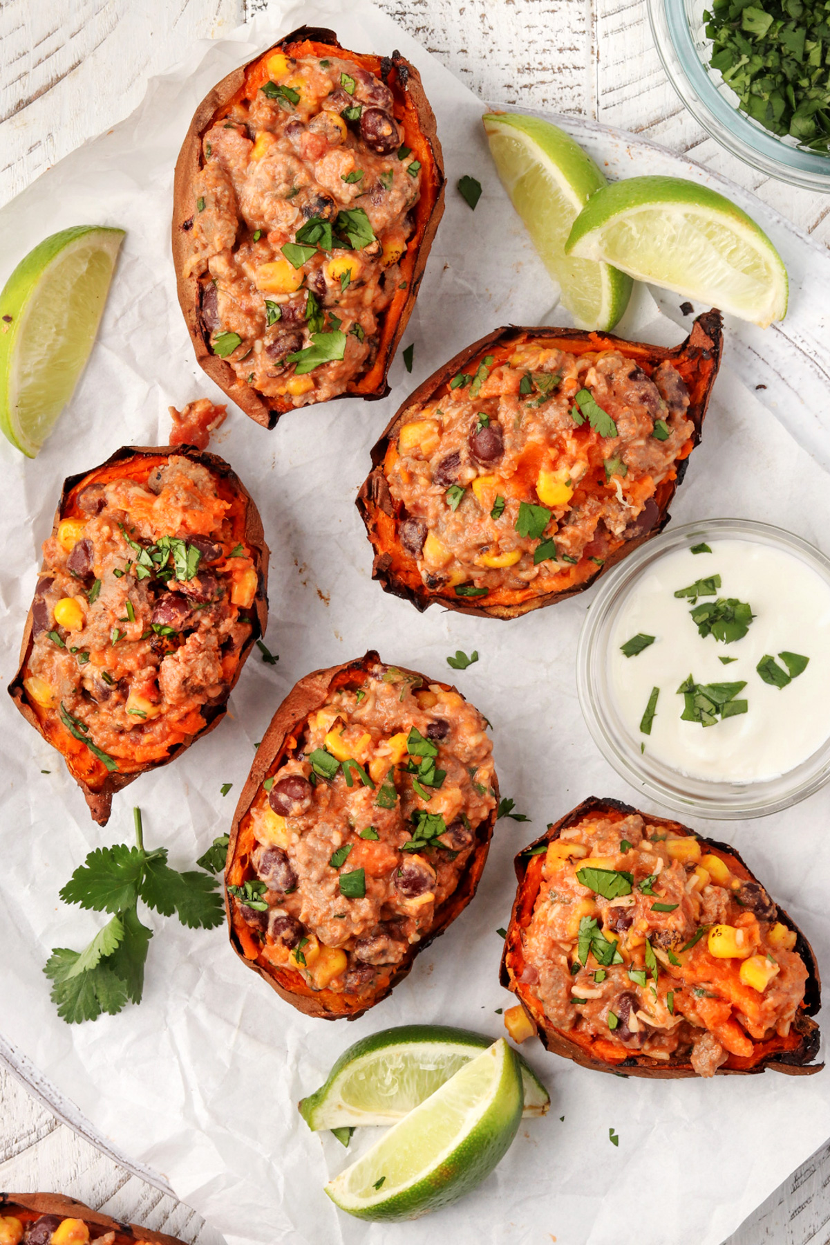 Baked Mexican Potatoes on a white plate with sour cream, limes and cilantro.