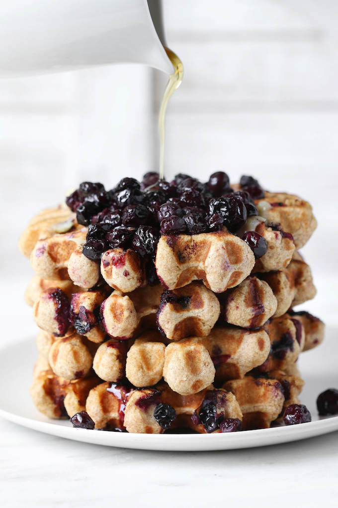 Whole Wheat Blueberry Oat Waffles stacked and topped with fresh blueberries and syrup.
