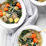 Roasted Potato, Sausage and Kale Soup in a white bowl on a marble countertop.