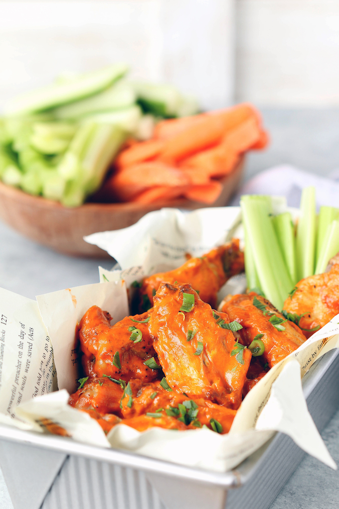 Extra Crispy Air Fryer Buffalo Chicken Wings in a silver basket lined with newspaper. Celery and carrots in a wooden bowl arranged in background.