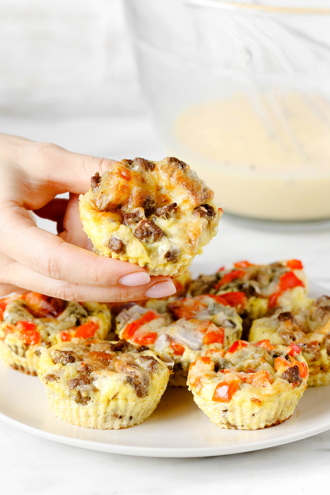 Freezer-Friendly Baked Egg Cupson a plate. A hand is picking up the one from the top center.