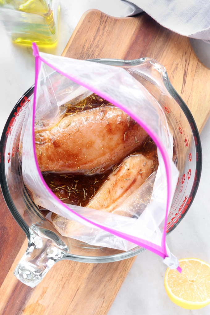 Simple Spiced Balsamic Chicken Marinade covering 3 chicken breasts. Chicken and marinade are inside of a plastic zipper bag that is sitting in a glass Pyrex bowl.