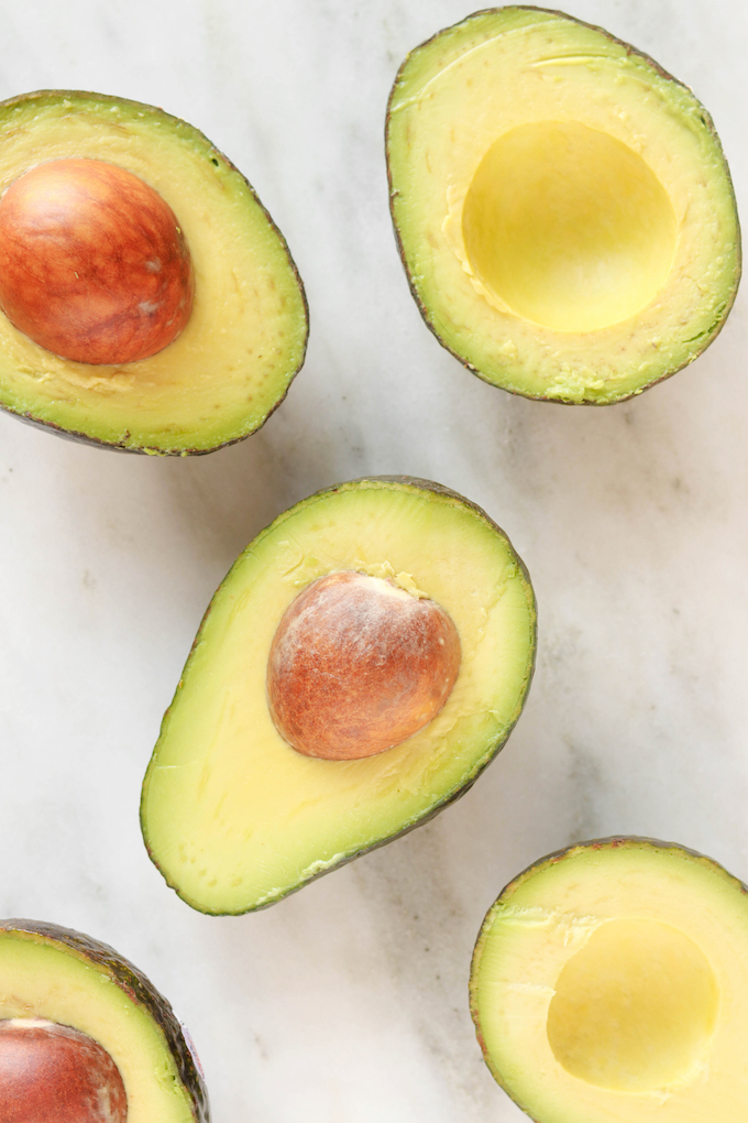 Sliced Avocados. Some have pits and some don't. All are arranged on a white marble countertop.