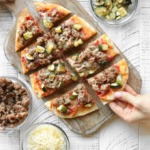 Chicken Sausage Flatbread Pizza on a wooden cutting board surrounded by pizza toppings.