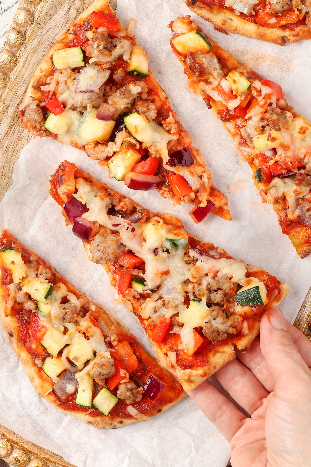 A hand reaching for a slice of Italian Sausage Flatbread Pizza.