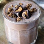Peanut Butter Cup Protein Smoothie in a glass cup. It is garnished with granola and peanut butter cups.