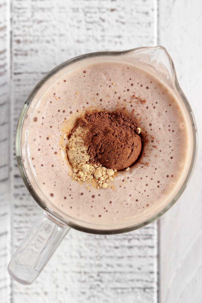 Peanut Butter Cup Protein Smoothie in a glass. Cocoa powder and peanut butter powder are ready to be mixed in.