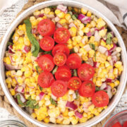 Easy Corn Salad in a white bowl and garnished with basil and cherry tomatoes.