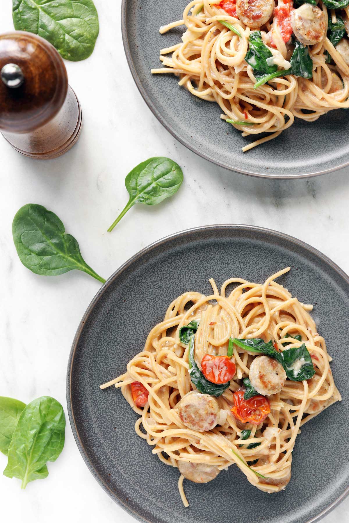 2 gray plates on a white countertop. Both plates are filled with chicken sausage pasta with garlic and lemon.