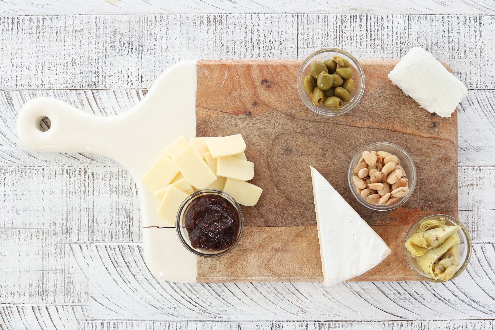 Cutting board with almonds, olives, artichokes, fig butter, brie, goat cheese and cheddar cheese.