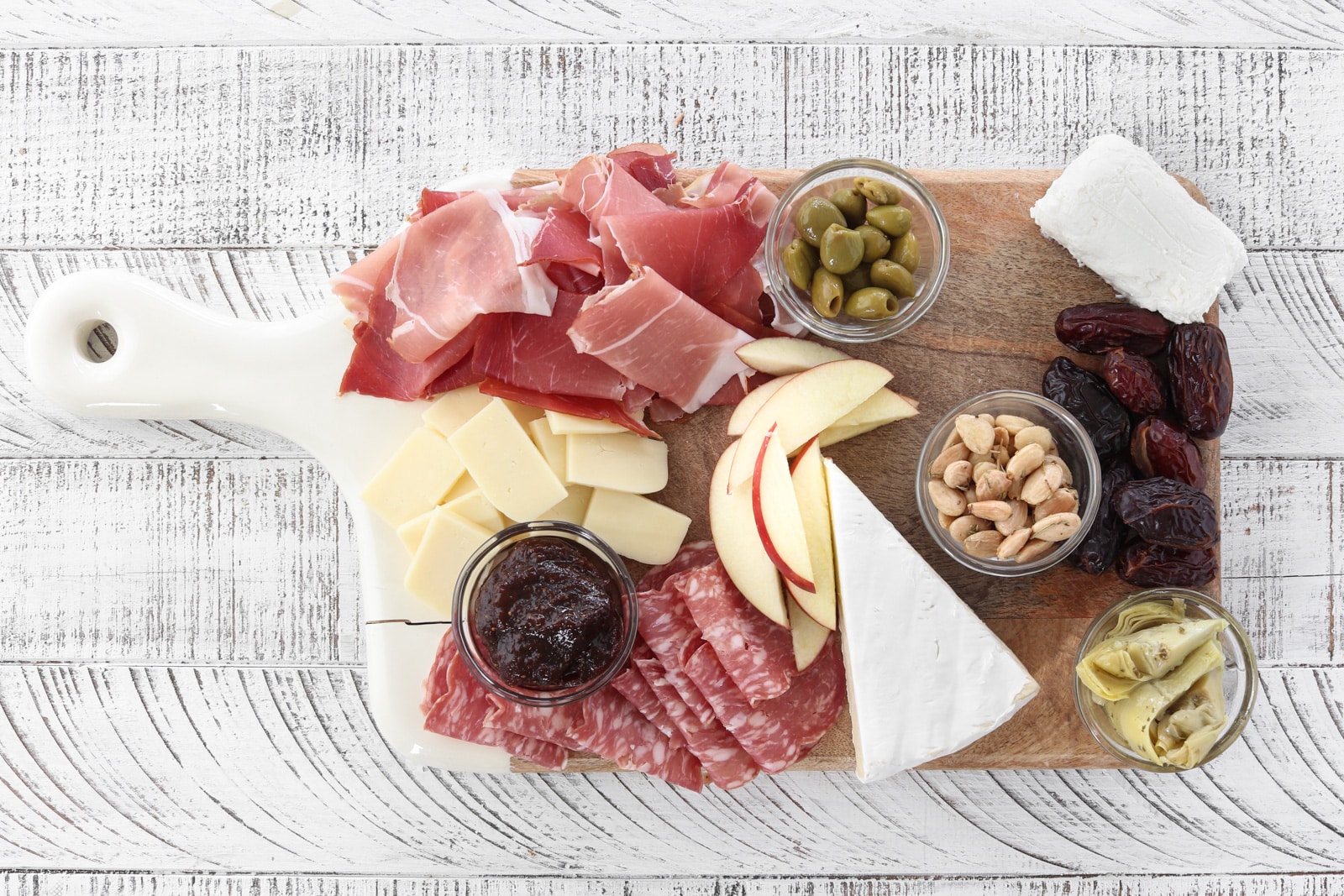 Cutting board with almonds, artichokes, cheeses, smoked meats, apples, fig butter  and dates.