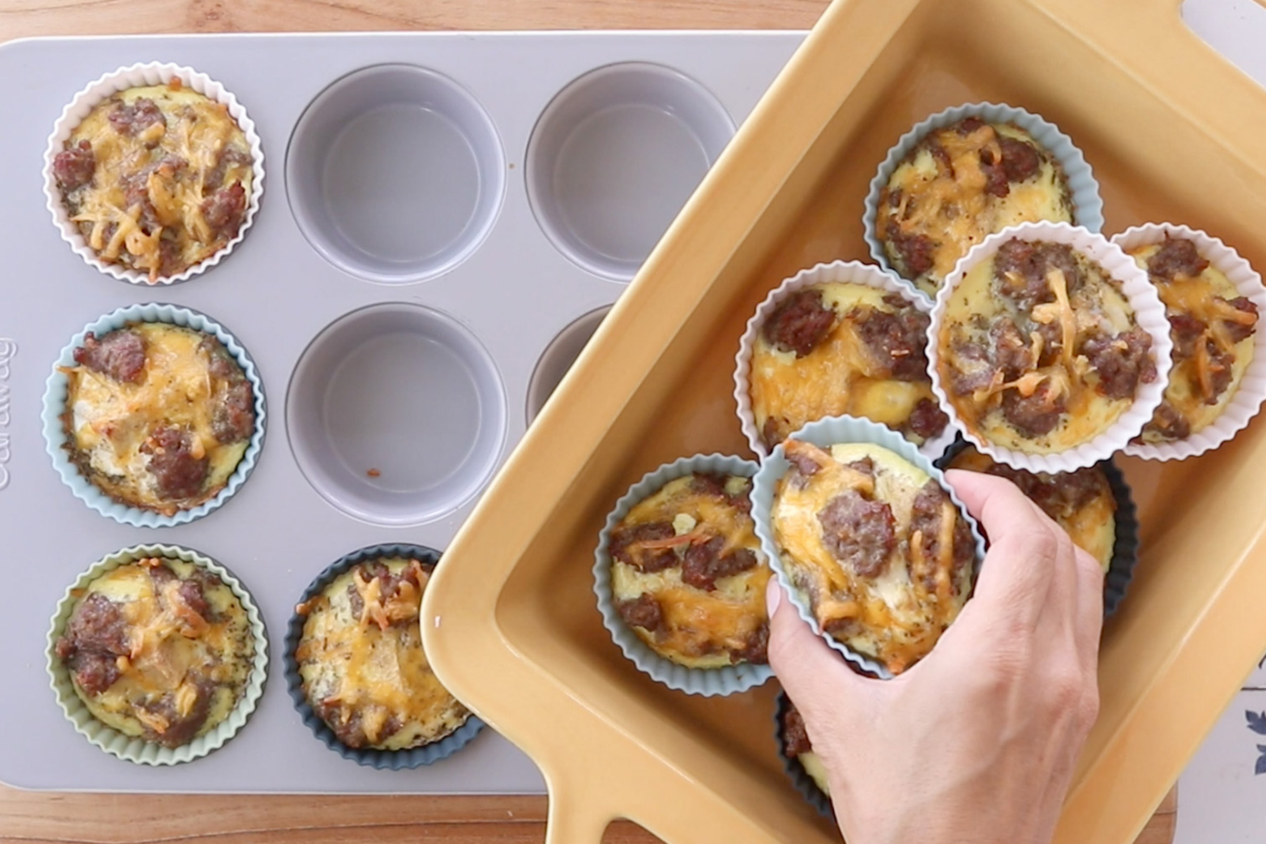 Hand transferring sausage and cheese egg muffins from a muffin pan to a tray to cool before freezing.