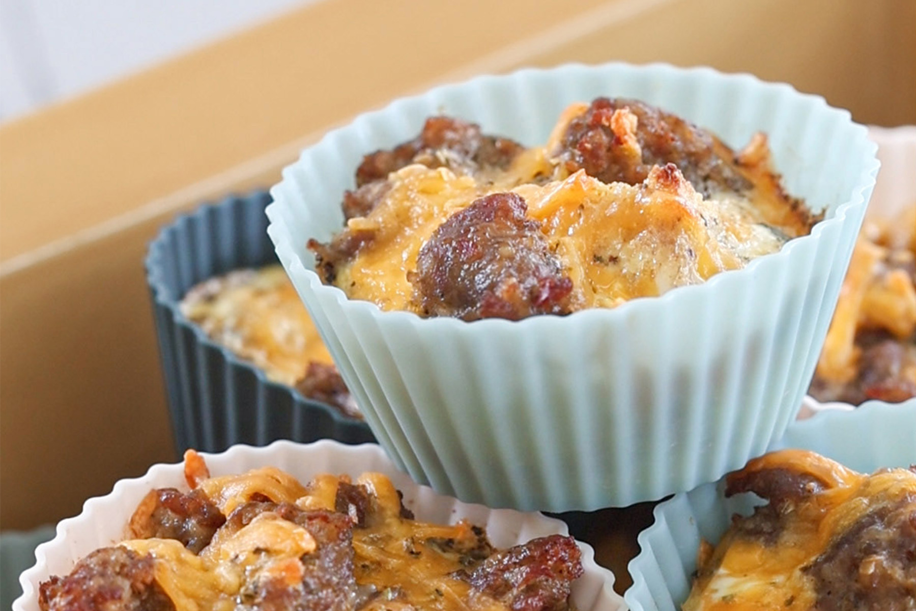 Close-up of sausage and cheese egg muffins in pastel silicone baking cups, ready to reheat.