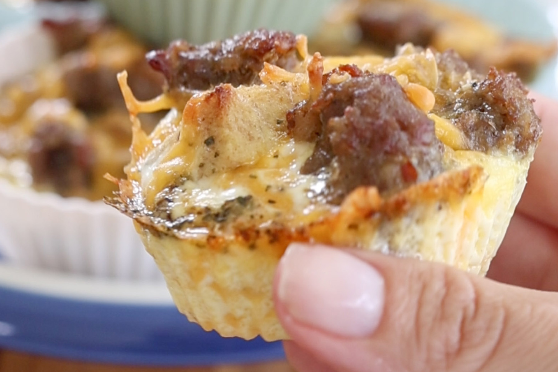 Hand holding a reheated sausage and cheese egg muffin with the silicone liner removed.