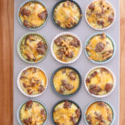 Hands holding a tray of sausage and cheese egg muffins baked in colorful silicone cups.