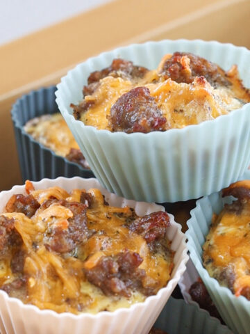 Freezer-friendly sausage and cheese egg muffins stacked in silicone baking cups inside a yellow cooler.